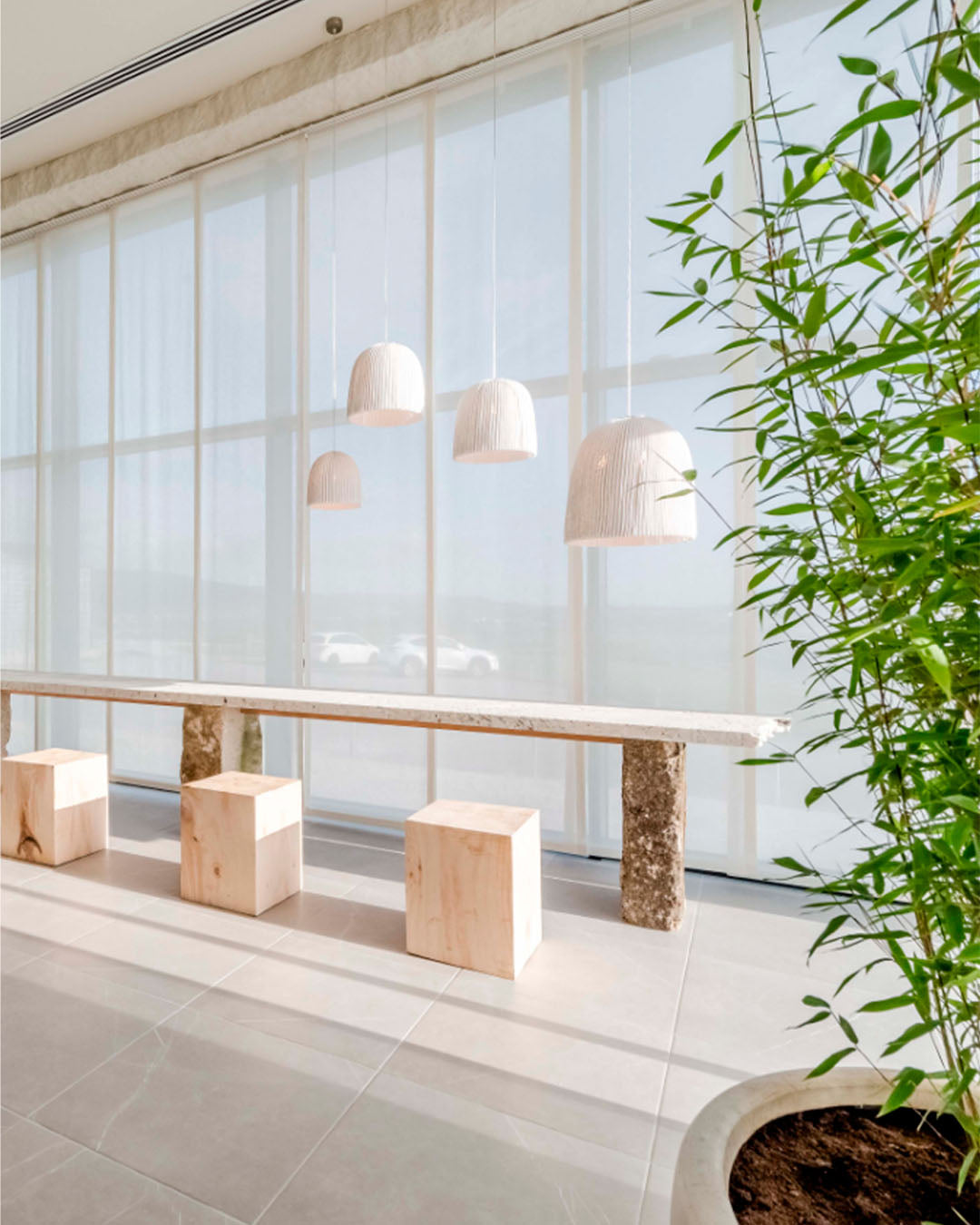 Lámparas colgantes modernas sobre mesa de madera con bancos cúbicos en espacio luminoso.