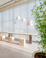Lámparas colgantes modernas sobre mesa de madera con bancos cúbicos en espacio luminoso.