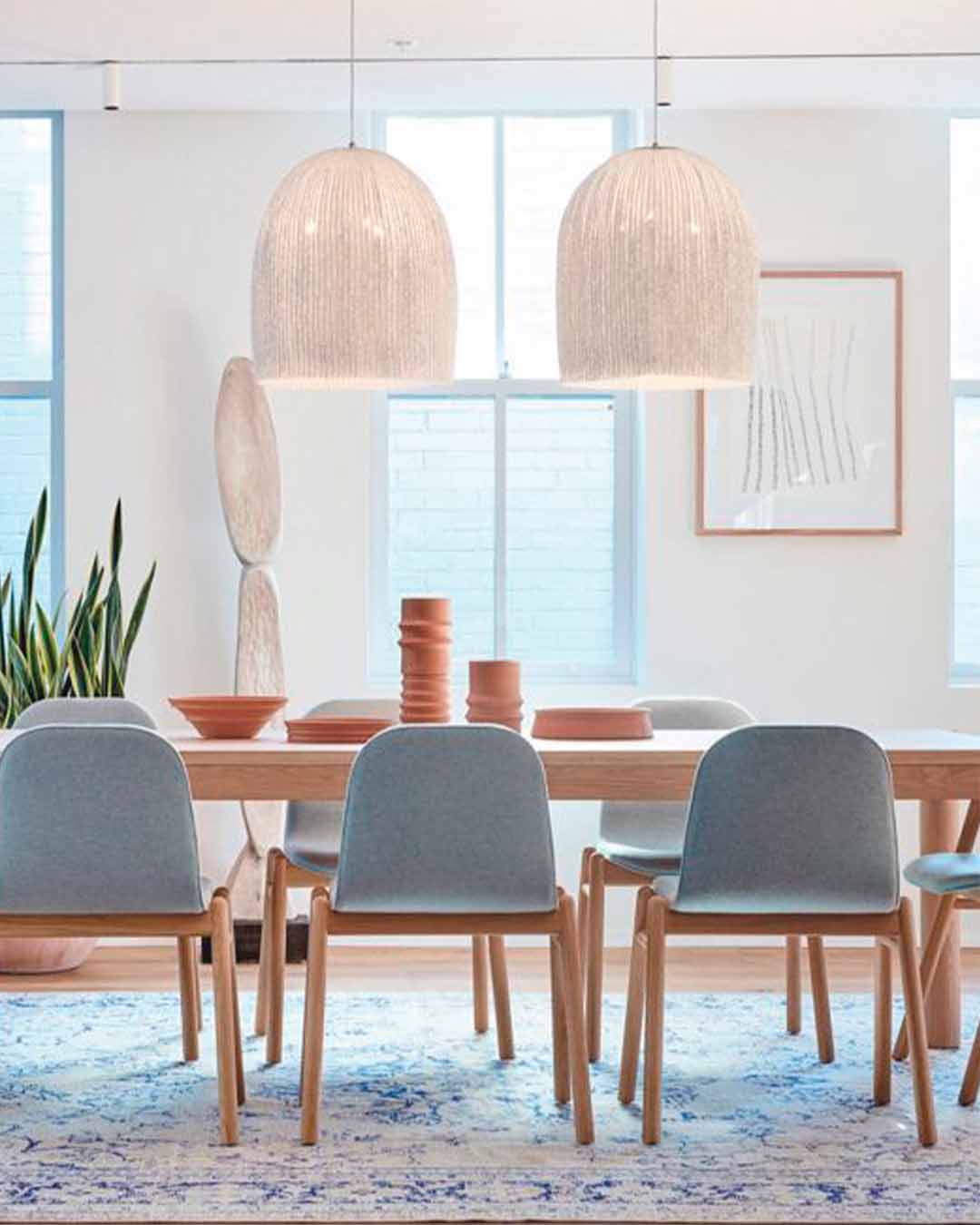 Lámparas colgantes de mimbre sobre mesa de comedor moderna con sillas grises, decoración minimalista.