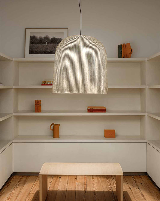 Lámpara colgante de diseño moderno iluminando sala minimalista con estantes y mesa de madera.