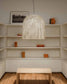 Lámpara colgante de diseño moderno iluminando sala minimalista con estantes y mesa de madera.