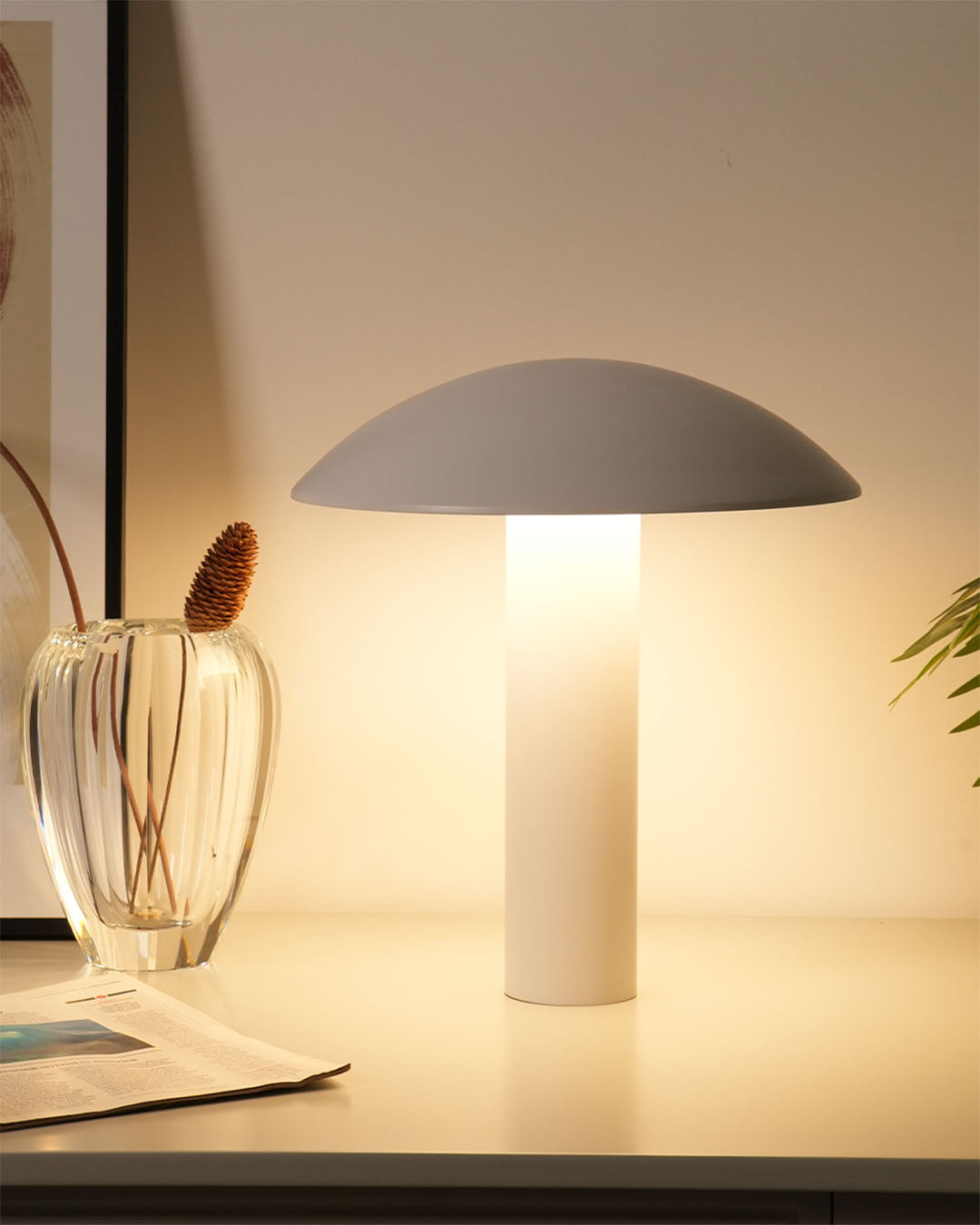 Lámpara de mesa moderna blanca encendida sobre escritorio con jarrón decorativo y planta
