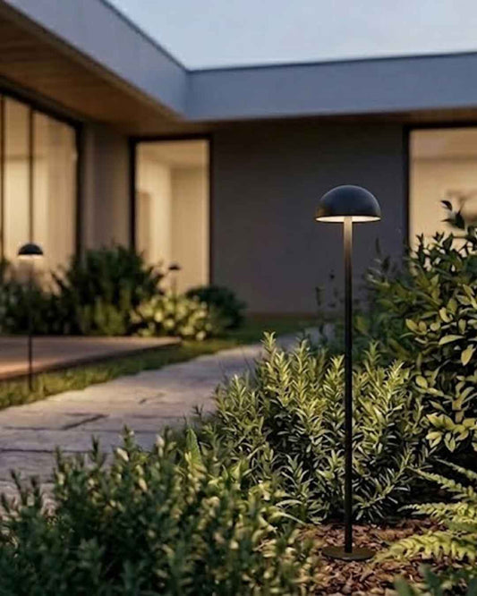 Lámpara exterior Setto Mini Outdoor negra con luz cálida LED en jardín residencial.