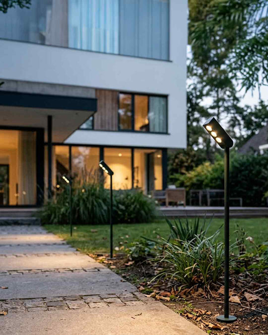 Luminaria estaca LED de exterior Slim Path negra iluminando camino de jardín residencial.