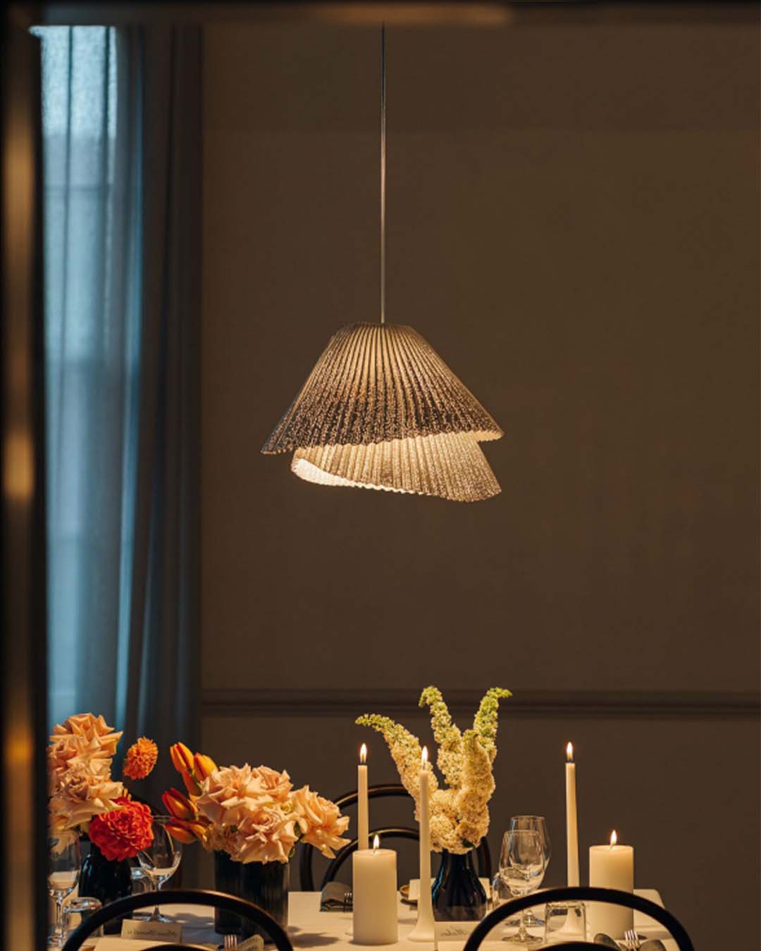 Lámpara colgante de diseño moderno sobre mesa de comedor con velas y flores elegantes