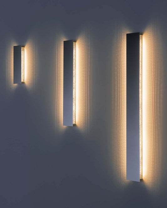 Aplique de pared lineal Umbra Line de a-emotional light en malla de acero con luz cálida e indirecta.