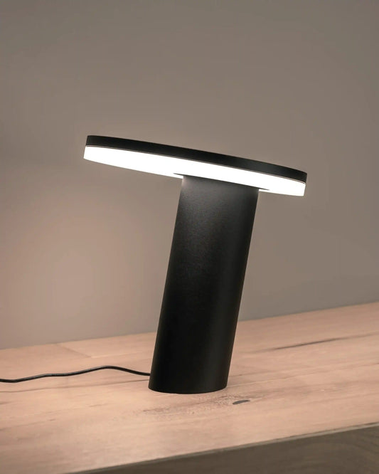 Lámpara de mesa moderna negra iluminada sobre superficie de madera, Birot MX iluminación.