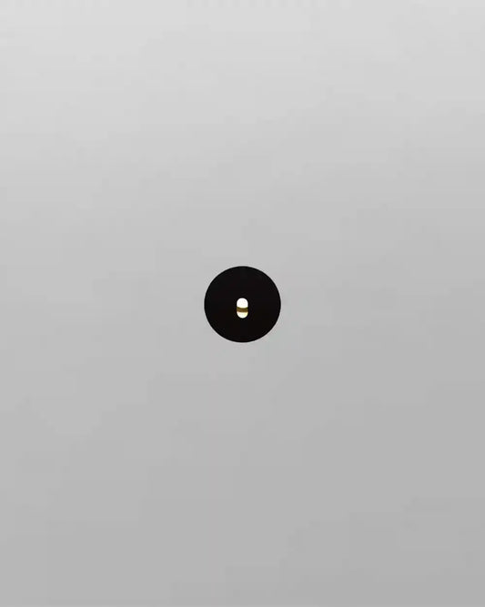 Aplique de pared negro minimalista encendido sobre fondo blanco, diseño moderno de iluminación.