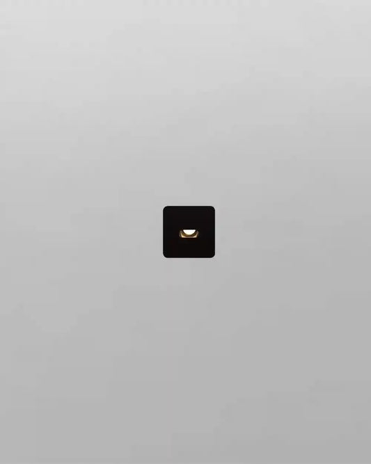 Aplique de pared cuadrado negro moderno encendido sobre fondo gris, iluminación Birot MX.