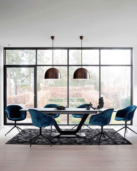 Comedor moderno con lámparas colgantes metálicas, sillas azules y ventanales, Birot MX iluminación.
