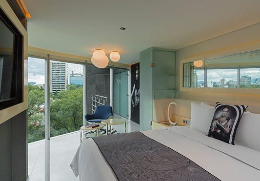 Habitación moderna con grandes ventanales, cama decorada y lámpara de techo esférica.