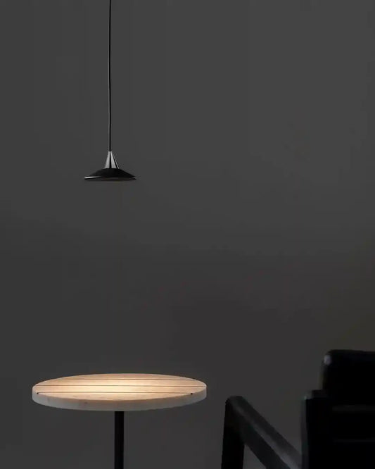 Lámpara colgante negra moderna sobre mesa redonda y sillón, iluminación minimalista Birot MX.