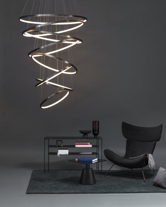 Lámpara colgante de aros LED modernos en sala minimalista con sillón y mesa negra.
