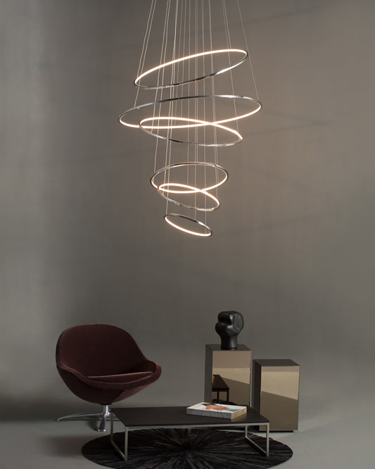 Lámpara colgante moderna de aros LED en sala minimalista con sillón y mesa decorativa.