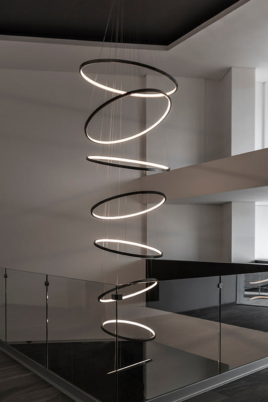 Lámpara colgante moderna de anillos LED sobre escalera, iluminación decorativa interior.