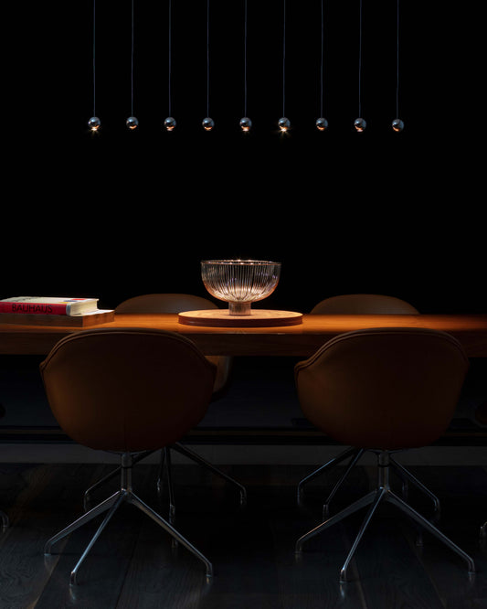 Lámpara colgante de bolas metálicas sobre mesa de comedor moderna con sillas marrones.