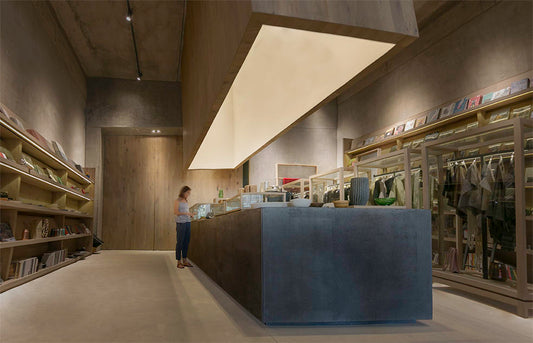 Tienda boutique moderna con iluminación cálida y estantes de madera, mujer en el mostrador.