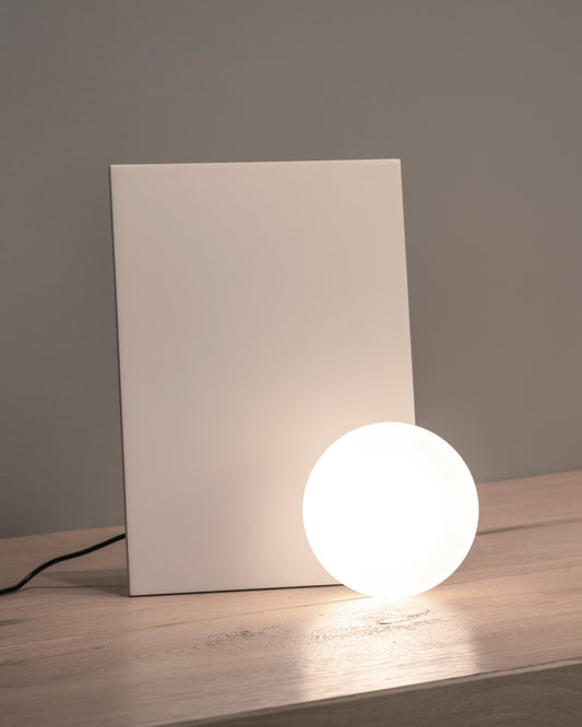 Lámpara de mesa moderna con esfera luminosa y base rectangular blanca sobre superficie de madera.