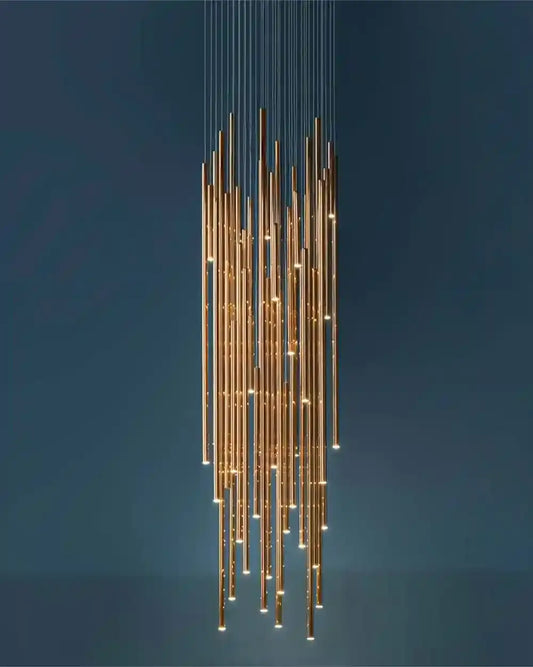 Lámpara colgante moderna de tubos dorados, iluminación decorativa Birot MX sobre fondo azul.