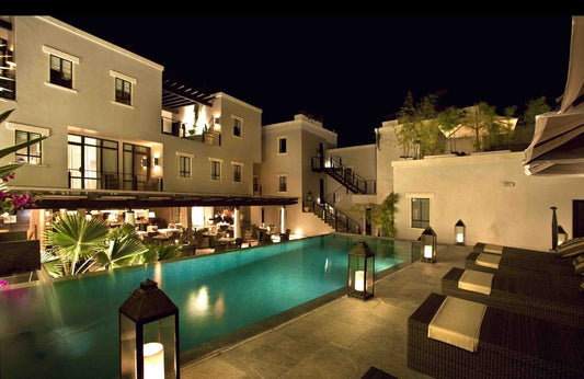 terraza nocturna con alberca iluminada, faroles decorativos y chaise longues en hotel moderno